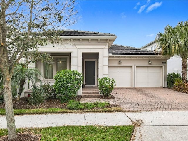 view of front of home featuring a garage, decorative driveway, a tiled roof, and stucco siding