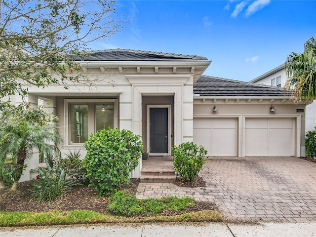 view of front of property with a garage, decorative driveway, a tile roof, and stucco siding