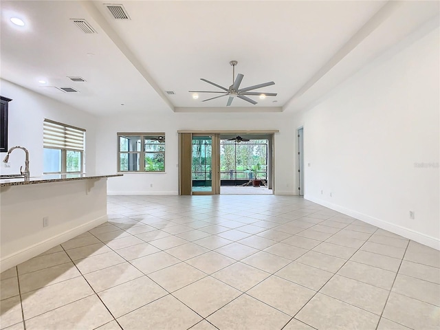 empty room featuring light tile patterned floors, a raised ceiling, visible vents, a healthy amount of sunlight, and a sink