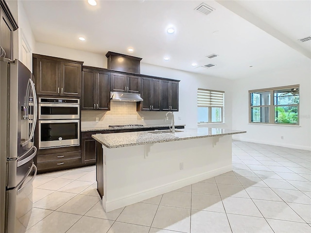 kitchen with light tile patterned floors, under cabinet range hood, a breakfast bar, appliances with stainless steel finishes, and tasteful backsplash