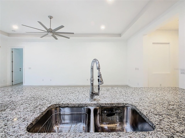 interior details with a tray ceiling, stone countertops, a sink, and a ceiling fan