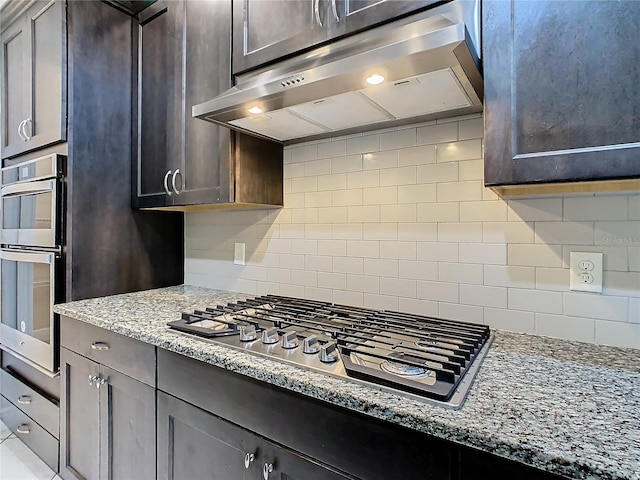 kitchen with stainless steel appliances, dark brown cabinets, under cabinet range hood, and decorative backsplash