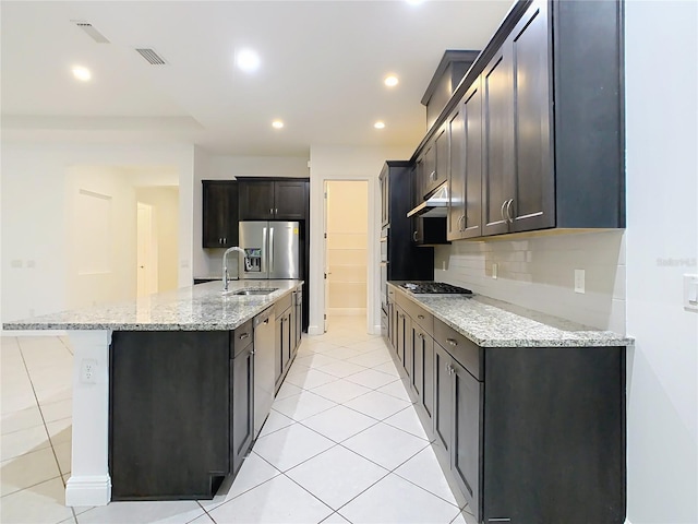 kitchen with light stone counters, a sink, stainless steel appliances, under cabinet range hood, and backsplash