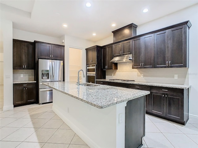 kitchen with light tile patterned floors, appliances with stainless steel finishes, dark brown cabinetry, light stone countertops, and under cabinet range hood