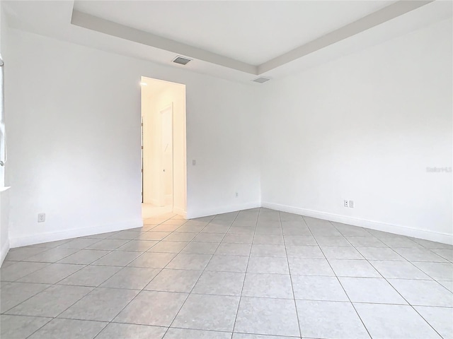 spare room with a raised ceiling, visible vents, baseboards, and light tile patterned floors