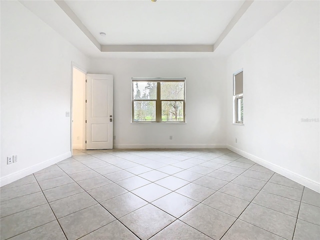 empty room with a wealth of natural light, a tray ceiling, and baseboards