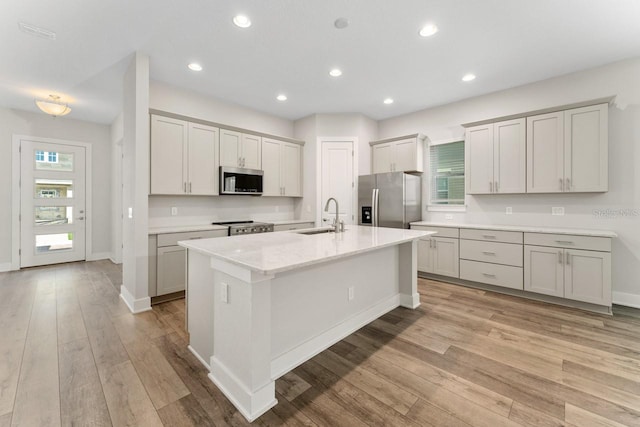 kitchen with light hardwood / wood-style floors, light stone countertops, stainless steel appliances, a center island with sink, and sink