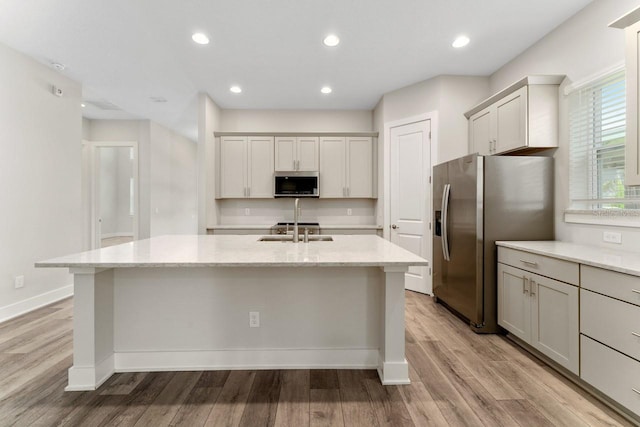 kitchen featuring stainless steel appliances, a center island with sink, and light wood-type flooring