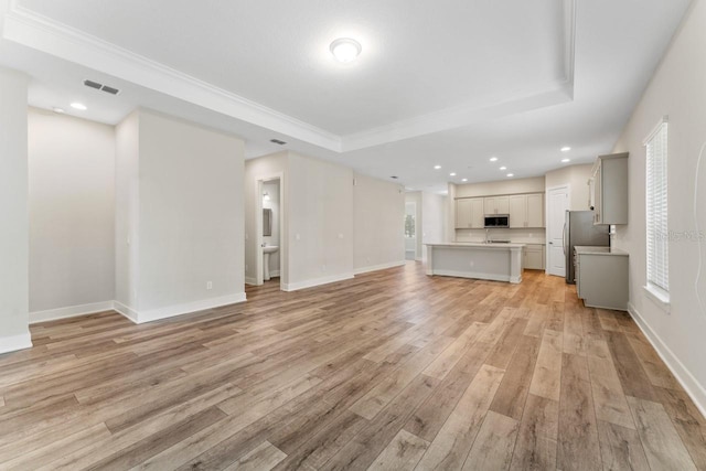 unfurnished living room featuring light hardwood / wood-style flooring, a raised ceiling, and crown molding