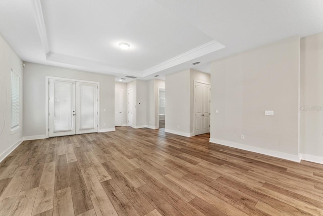 unfurnished living room with french doors, light wood-type flooring, and a raised ceiling