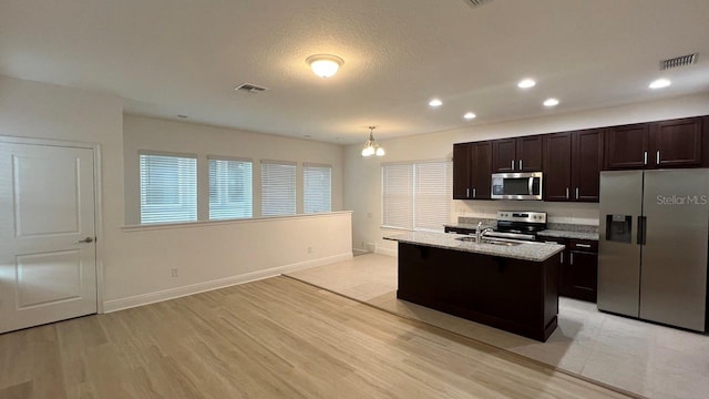 kitchen with light wood-type flooring, an island with sink, hanging light fixtures, an inviting chandelier, and stainless steel appliances