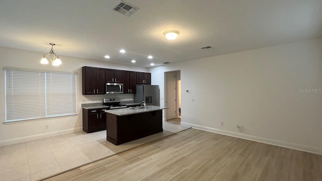 kitchen with appliances with stainless steel finishes, an inviting chandelier, decorative light fixtures, dark brown cabinetry, and a kitchen island with sink