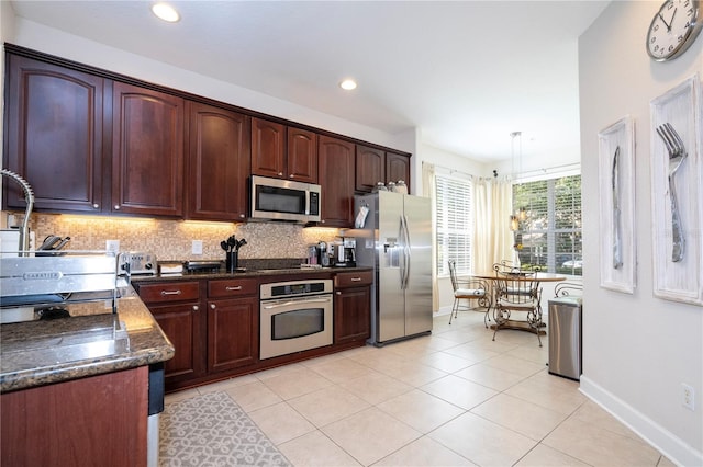 kitchen featuring light tile patterned flooring, hanging light fixtures, decorative backsplash, appliances with stainless steel finishes, and dark stone countertops