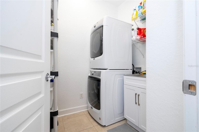 washroom with light tile patterned floors, cabinets, and stacked washer / drying machine