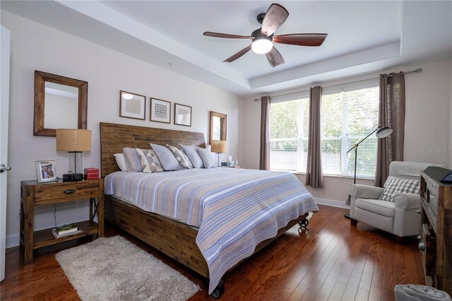 bedroom featuring a raised ceiling, dark hardwood / wood-style flooring, and ceiling fan