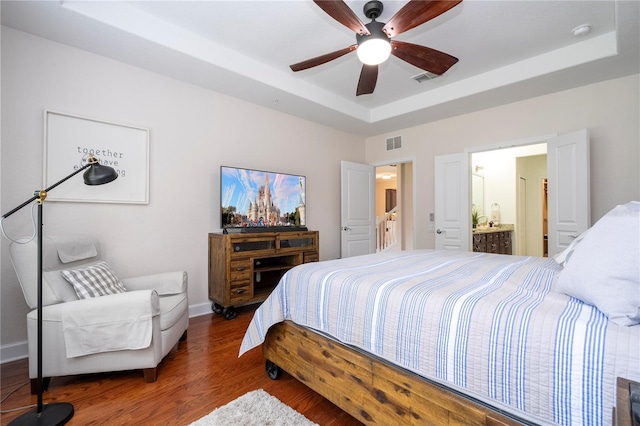 bedroom featuring a tray ceiling, ceiling fan, ensuite bathroom, and dark wood-type flooring