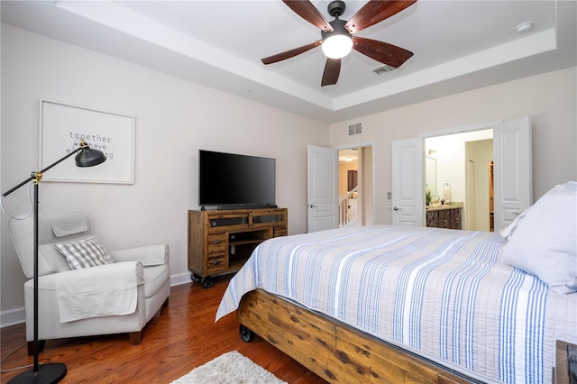 bedroom with connected bathroom, a tray ceiling, ceiling fan, and dark hardwood / wood-style flooring