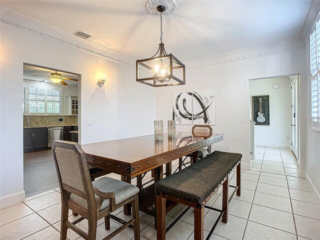 tiled dining space featuring a textured ceiling, ceiling fan with notable chandelier, and crown molding