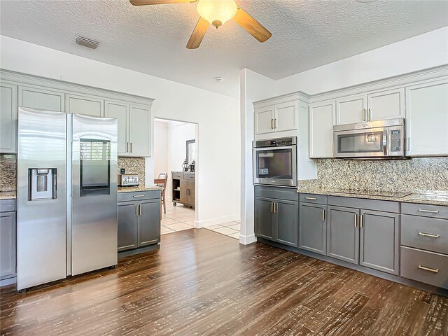 kitchen with gray cabinetry, ceiling fan, dark wood-type flooring, decorative backsplash, and appliances with stainless steel finishes