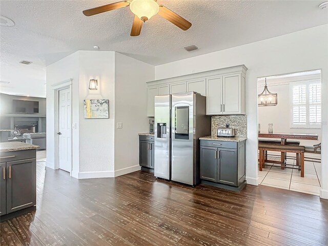 kitchen with gray cabinetry, stainless steel fridge, dark wood-type flooring, and ceiling fan with notable chandelier