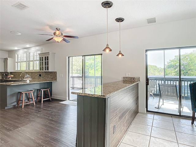 kitchen featuring stone counters, decorative backsplash, ceiling fan, decorative light fixtures, and kitchen peninsula