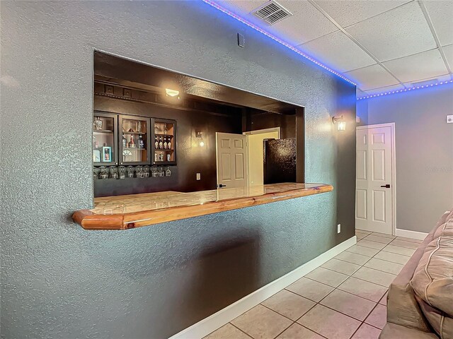 interior space with a paneled ceiling, black refrigerator, tile patterned flooring, and wood counters