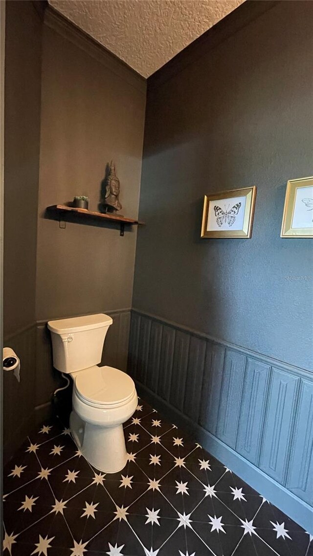 bathroom featuring tile patterned floors, toilet, ornamental molding, and a textured ceiling