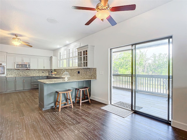 kitchen with kitchen peninsula, appliances with stainless steel finishes, backsplash, gray cabinetry, and a breakfast bar