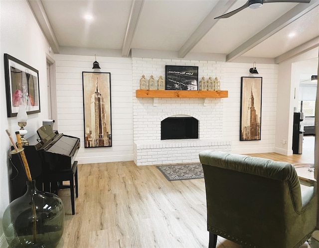 living room with ceiling fan, light hardwood / wood-style flooring, beamed ceiling, and a brick fireplace