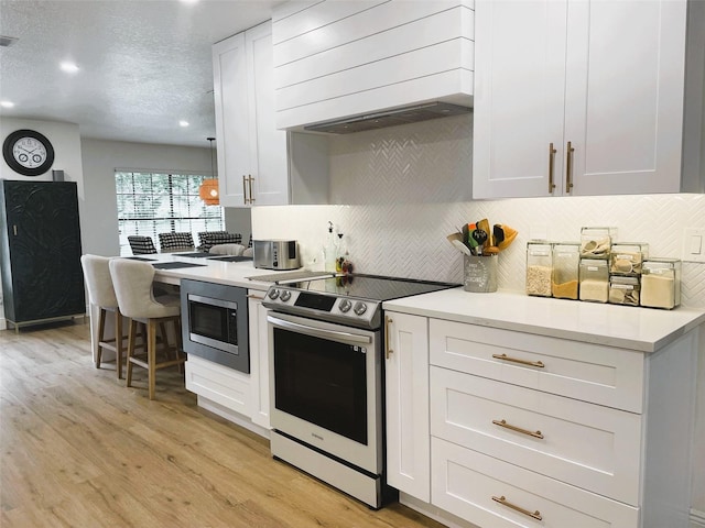 kitchen featuring light hardwood / wood-style floors, a textured ceiling, white cabinets, custom range hood, and appliances with stainless steel finishes