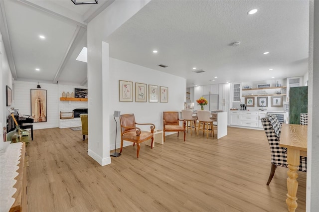 interior space with beamed ceiling, a textured ceiling, a brick fireplace, and light hardwood / wood-style flooring