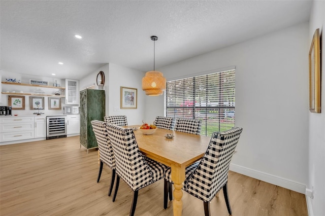 dining area featuring a textured ceiling, light hardwood / wood-style floors, and beverage cooler