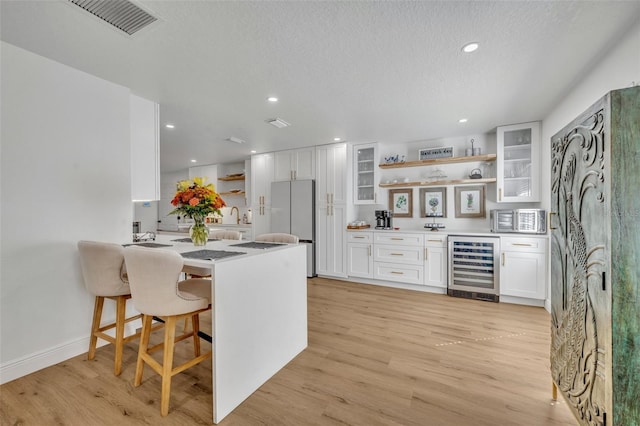 kitchen with a kitchen bar, beverage cooler, white refrigerator, light hardwood / wood-style floors, and white cabinetry