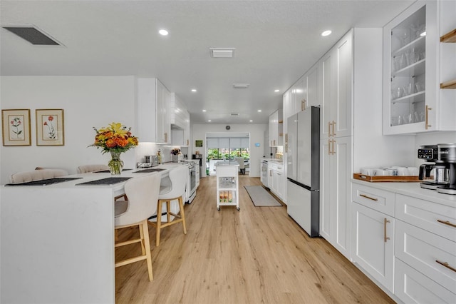 kitchen featuring white cabinets, light hardwood / wood-style floors, a kitchen bar, kitchen peninsula, and stainless steel refrigerator