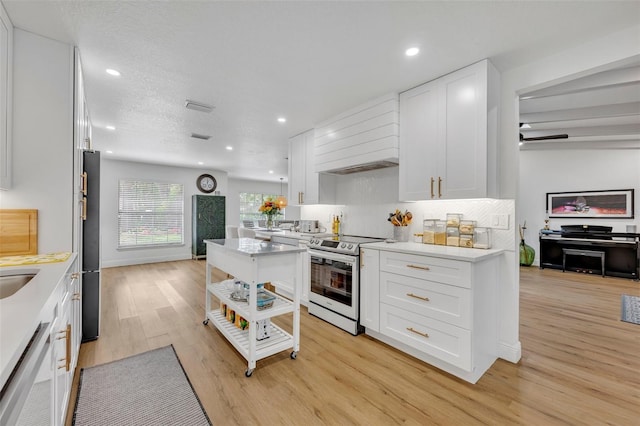 kitchen featuring light wood-type flooring, tasteful backsplash, custom exhaust hood, stainless steel appliances, and white cabinets