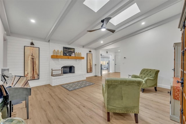 living room with a brick fireplace, ceiling fan, vaulted ceiling with skylight, and light wood-type flooring