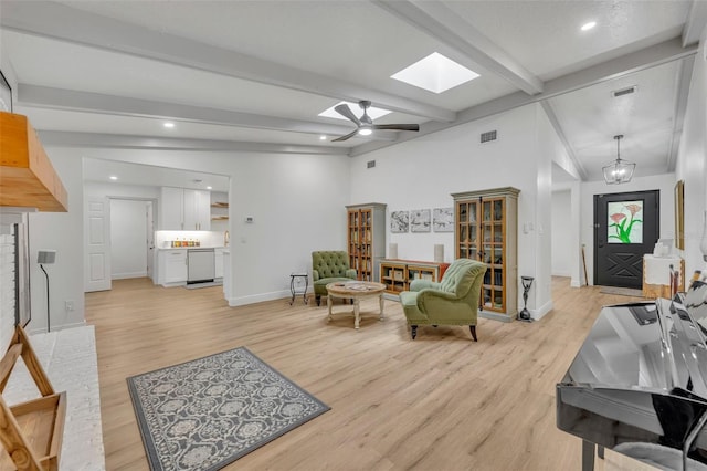 living room featuring ceiling fan, vaulted ceiling with skylight, and light wood-type flooring