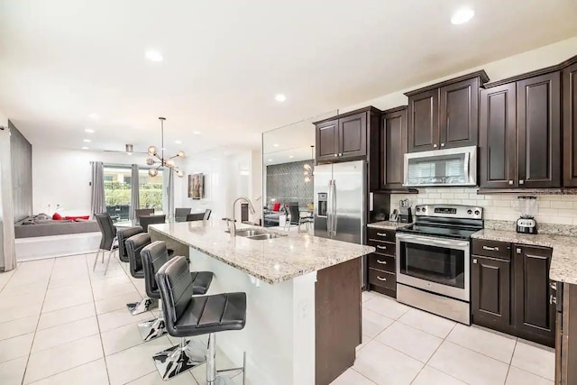 kitchen featuring sink, decorative light fixtures, a center island with sink, appliances with stainless steel finishes, and a breakfast bar