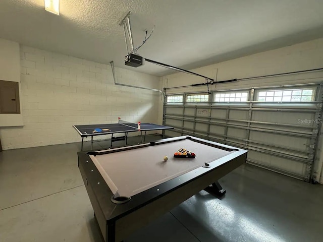 playroom with a textured ceiling, electric panel, concrete floors, concrete block wall, and a garage