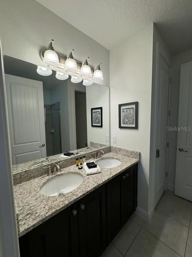 full bath with tile patterned flooring, a sink, double vanity, and a textured ceiling