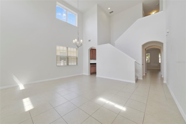 unfurnished living room with a high ceiling, a chandelier, a wealth of natural light, and light tile patterned flooring