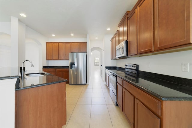 kitchen featuring dark stone countertops, sink, light tile patterned floors, and stainless steel appliances