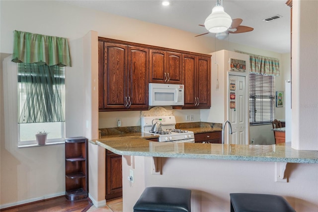 2366 Prairie Dunes, Clermont, FL 34711 - kitchen featuring white appliances, light stone counters, visible vents, ceiling fan, and a kitchen bar