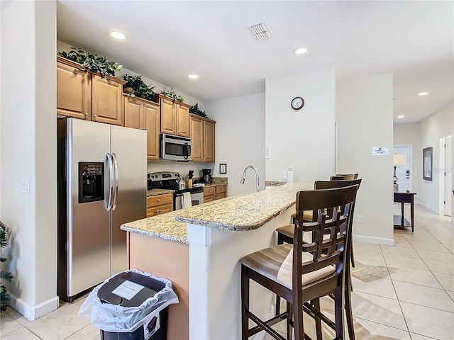 kitchen with appliances with stainless steel finishes, light tile patterned flooring, light stone counters, a breakfast bar, and kitchen peninsula