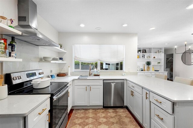 kitchen with white cabinets, sink, kitchen peninsula, wall chimney range hood, and appliances with stainless steel finishes