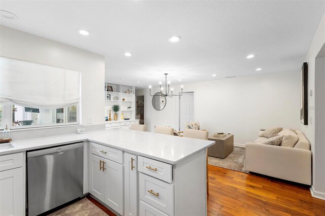 kitchen with wood-type flooring, dishwasher, white cabinets, kitchen peninsula, and an inviting chandelier