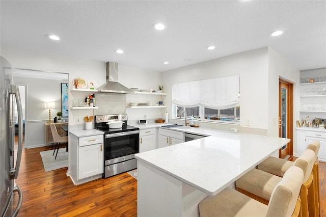 kitchen with appliances with stainless steel finishes, wall chimney exhaust hood, sink, and a kitchen breakfast bar