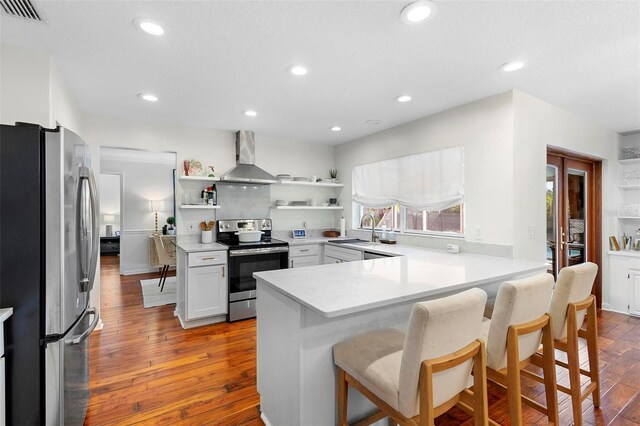 kitchen featuring appliances with stainless steel finishes, wood-type flooring, wall chimney exhaust hood, and kitchen peninsula