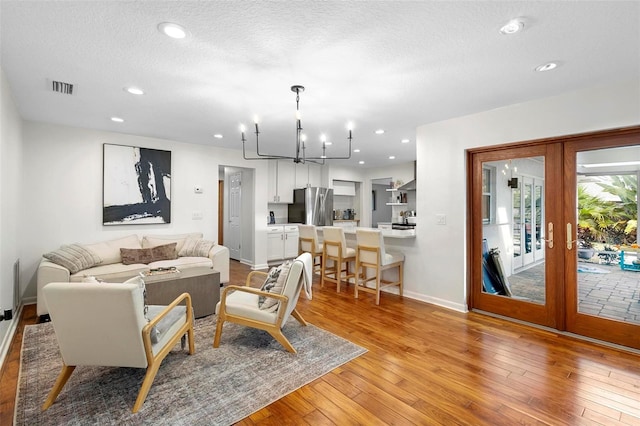 living room with light hardwood / wood-style flooring, a chandelier, a textured ceiling, and french doors