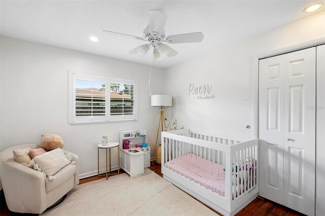 bedroom with a crib, wood-type flooring, and ceiling fan